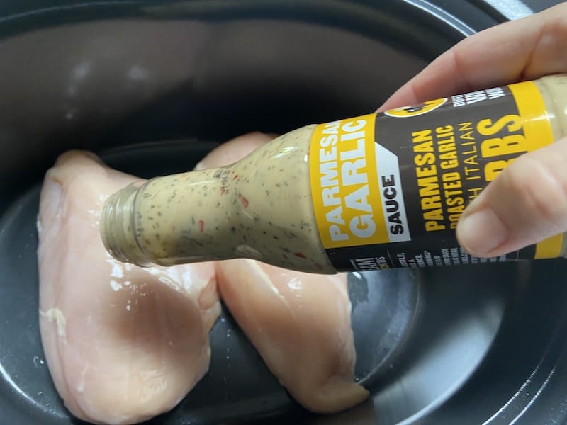 Step 2 - Chicken in a pot and a bottle of sauce poured into the pot.