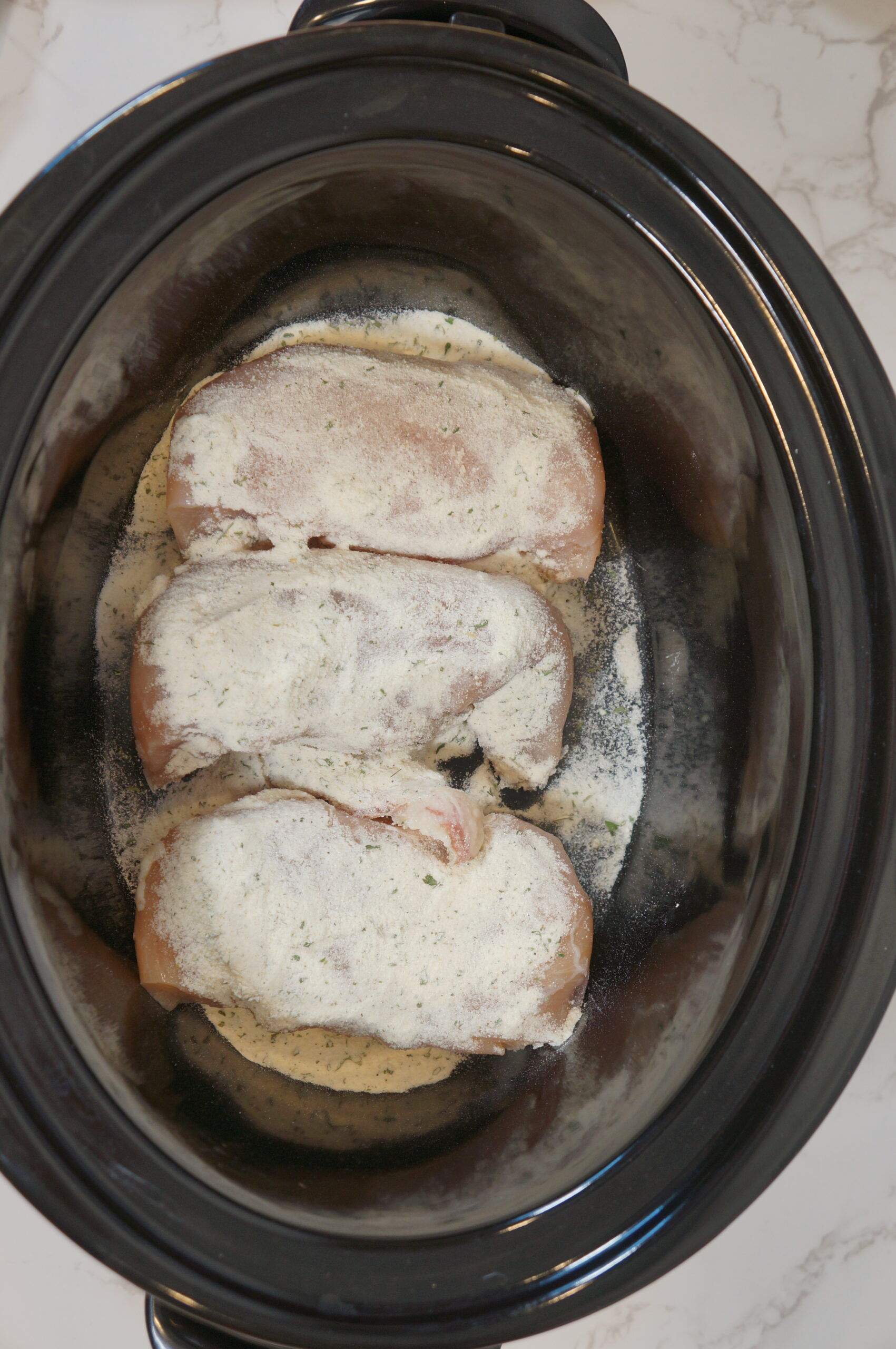 adding chicken to the crockpot with seasoning