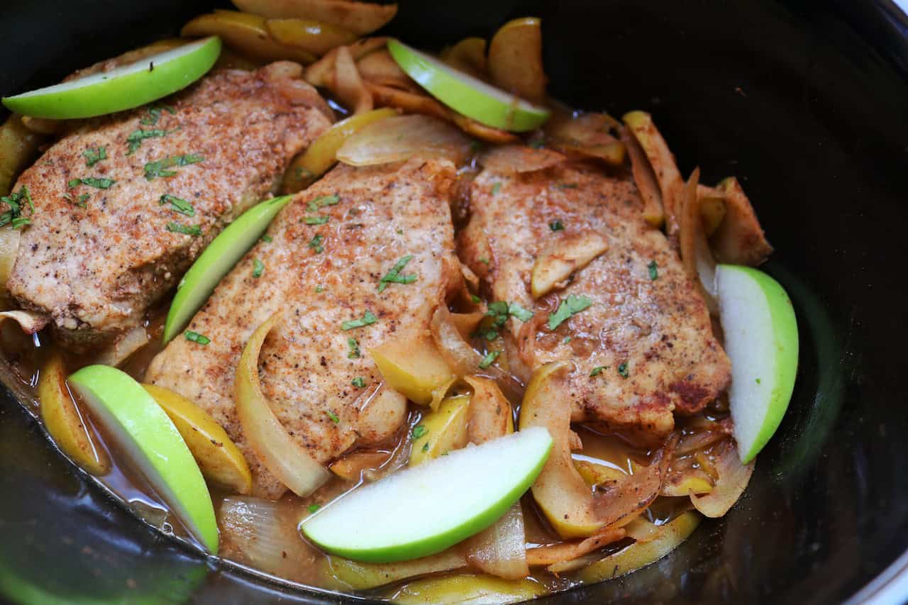 Cooked pork chops in crockpot with onions and apples and parsley garnish