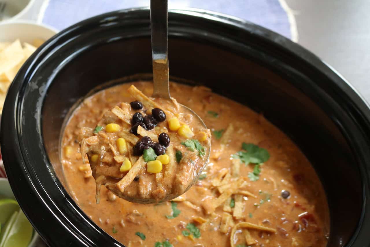 Chicken Chili Enchilada Soup in ladle with chips and limes.