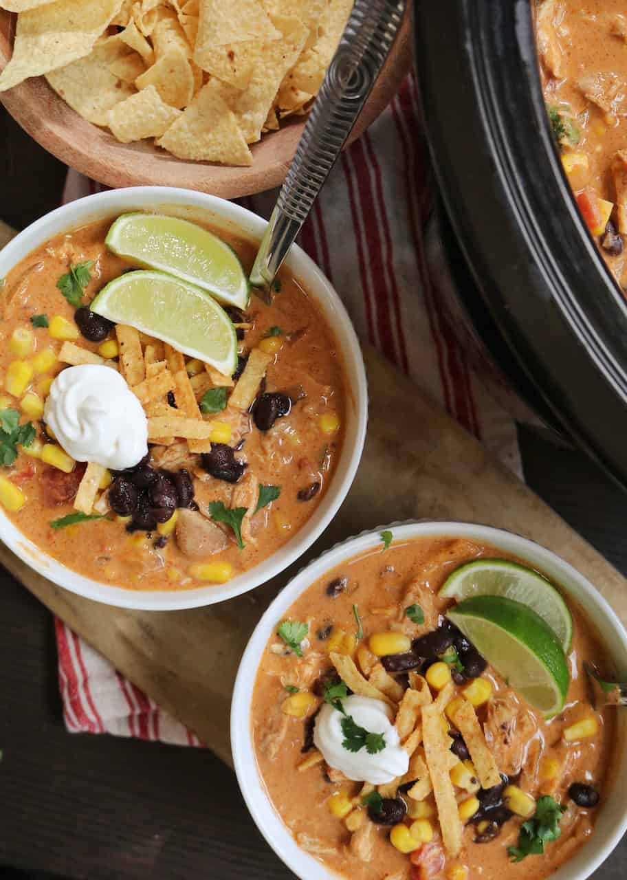 Two bowls of soup with limes and toppings.